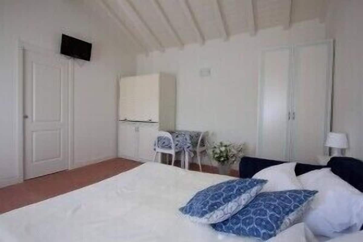 A bedroom with a bed, a chair, a desk, and a TV mounted on the wall.