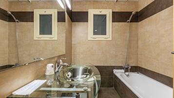 Een moderne badkamer met een wastafel met glazen ombouw, een bad en twee douchekoppen.