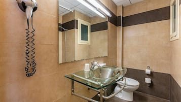 Un baño moderno con un lavabo de vidrio, un secador de pelo montado en la pared y un inodoro.