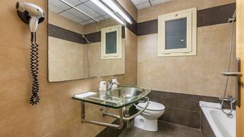 Un baño moderno con un lavabo de vidrio, inodoro, ducha y un secador de pelo montado en la pared.