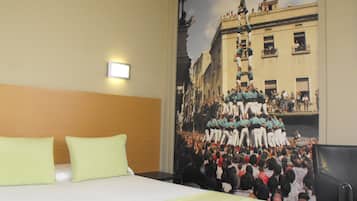 Habitación de hotel con cama, dos almohadas, una mesita de noche y un mural en la pared que representa un acontecimiento histórico.