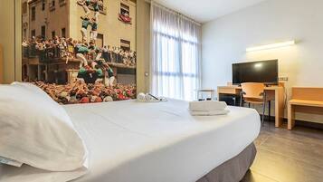 A hotel room with a large bed, a desk with a chair, a television, and a window with curtains.