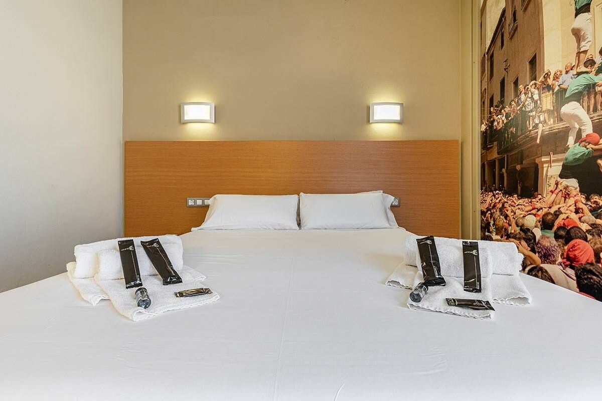 A hotel room with a large bed, two bedside tables, and a headboard. There are two wall-mounted lights above the bed.