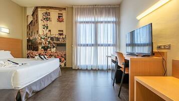 A hotel room with a bed, desk, chair, television, and a large window with curtains.