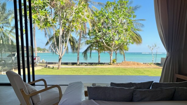 Un dormitorio con una cama grande, una silla y vista a la playa y al océano.
