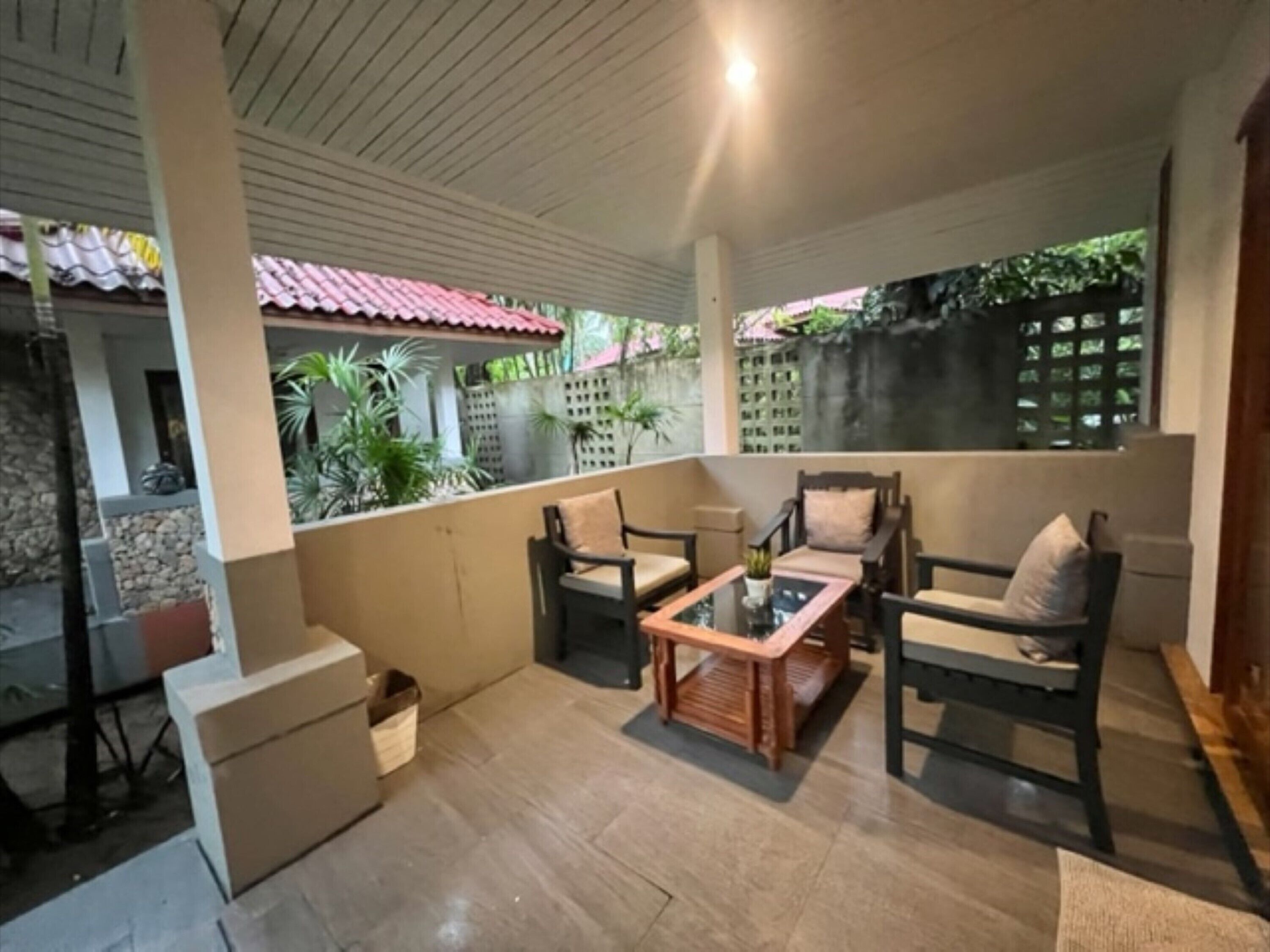 A covered patio with a table and chairs, surrounded by plants and a stone wall.