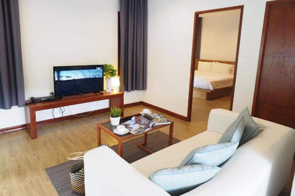 Ett modernt hotellrum med en soffa, ett soffbord, en TV, en säng och en spegel.