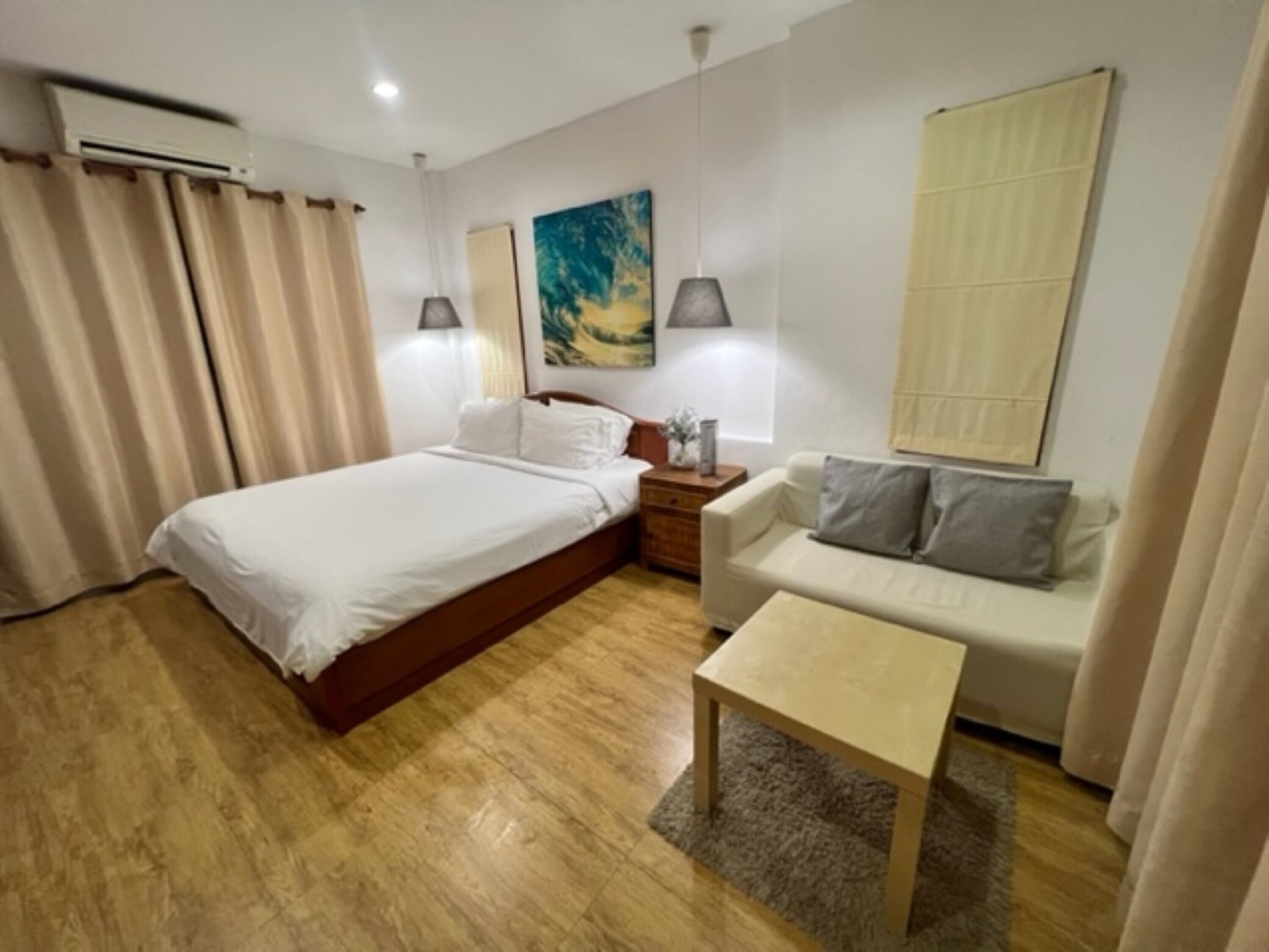 A hotel room with a bed, a sofa, a small table, and a painting on the wall.