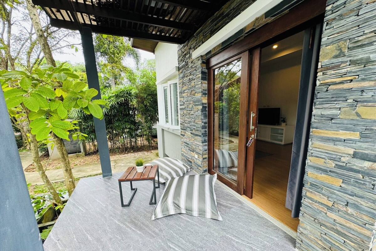 En modern uteplats med en stenmur, en träpergola och en skjutdörr i glas som leder in till ett köksområde.