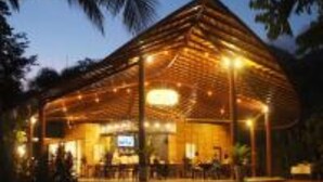 Una estructura de madera con techo curvo, posiblemente un restaurante o cafetería, con mesas al aire libre y una piscina al frente.