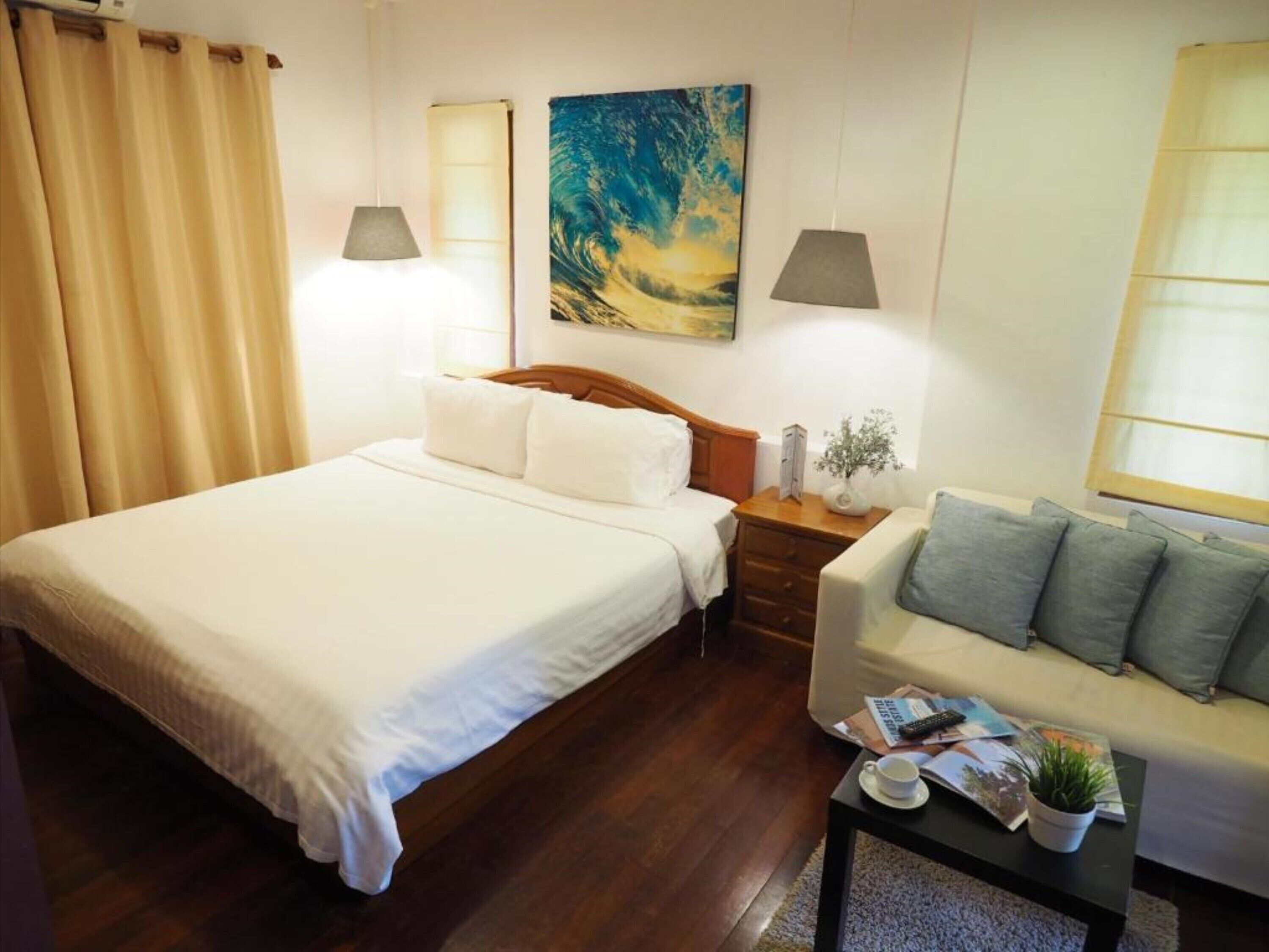 A hotel room with a large bed, a sofa, a nightstand with a lamp, and a painting on the wall.
