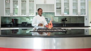 A chef cooking on a gas stove in a modern kitchen with white cabinetry and a black countertop. - Little Waters on the Cliff (Negril)
