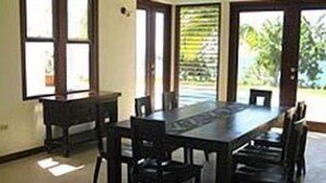 A dining area with a long table and chairs, large windows, and a view of greenery outside. - Little Waters on the Cliff (Negril)