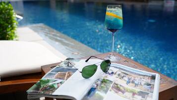 A poolside table with a drink, sunglasses, and a magazine.