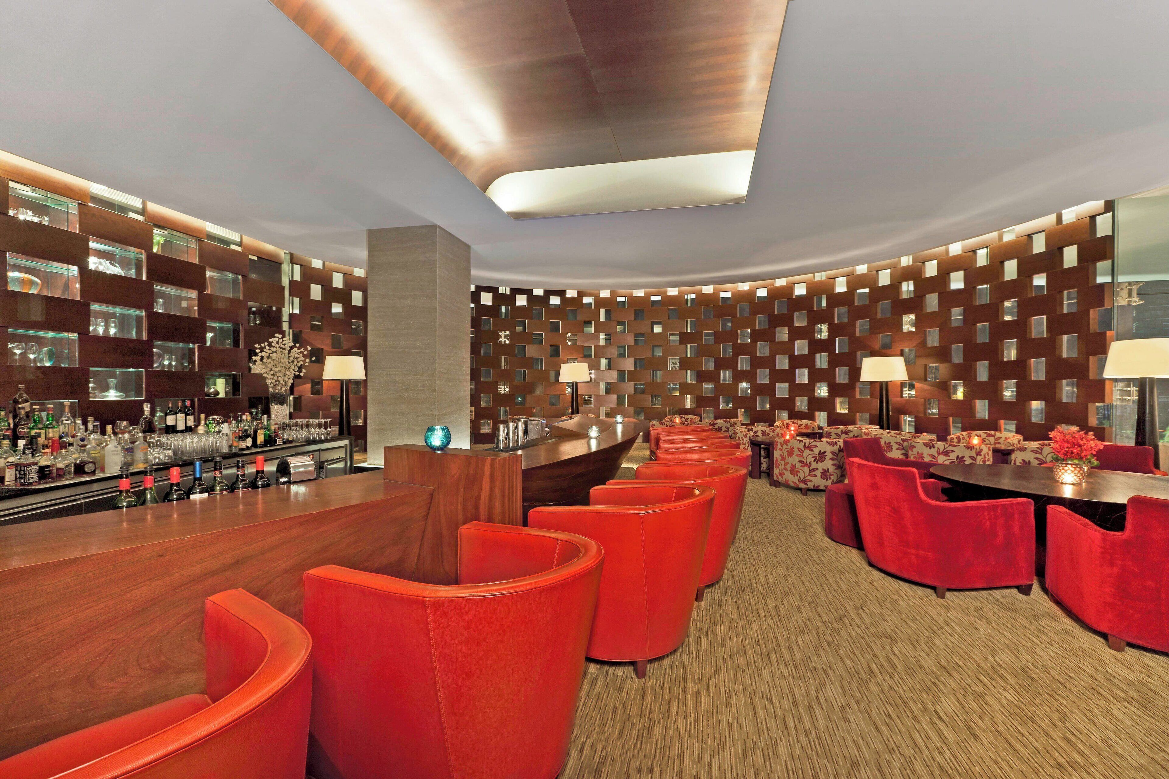 A modern bar area with red seating, a bar counter with a variety of bottles, and a patterned wall design.