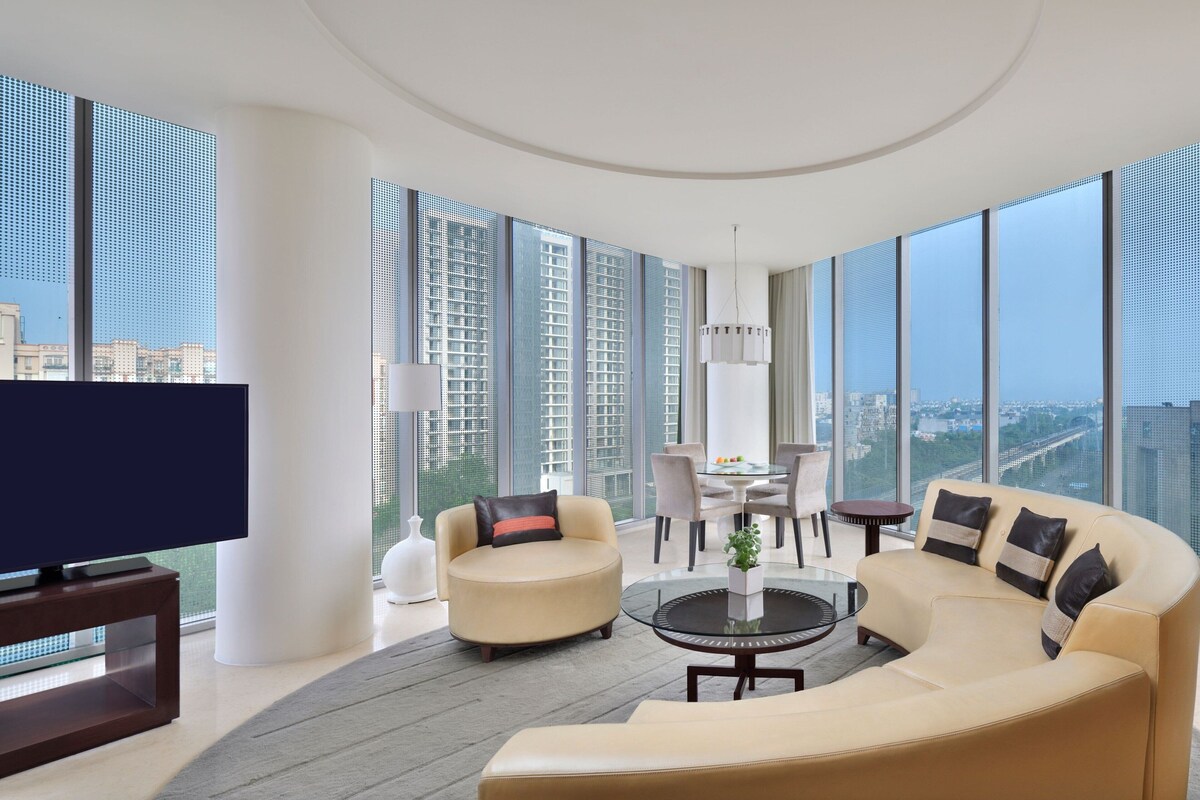 A modern living room with a curved sofa, a television, and a dining area with a table and chairs.