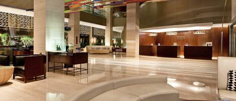 Un moderno vestíbulo de hotel con mostrador de recepción, zonas de estar y un techo decorativo.