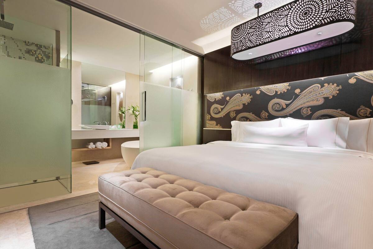 Quarto moderno com cama grande, closet envidraçado e cabeceira decorativa.