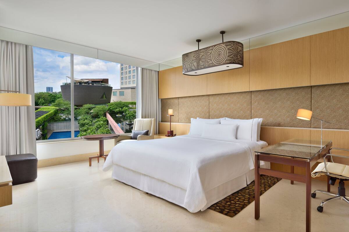 Quarto de hotel moderno com uma cama grande, uma mesa de trabalho e vista para a paisagem urbana.