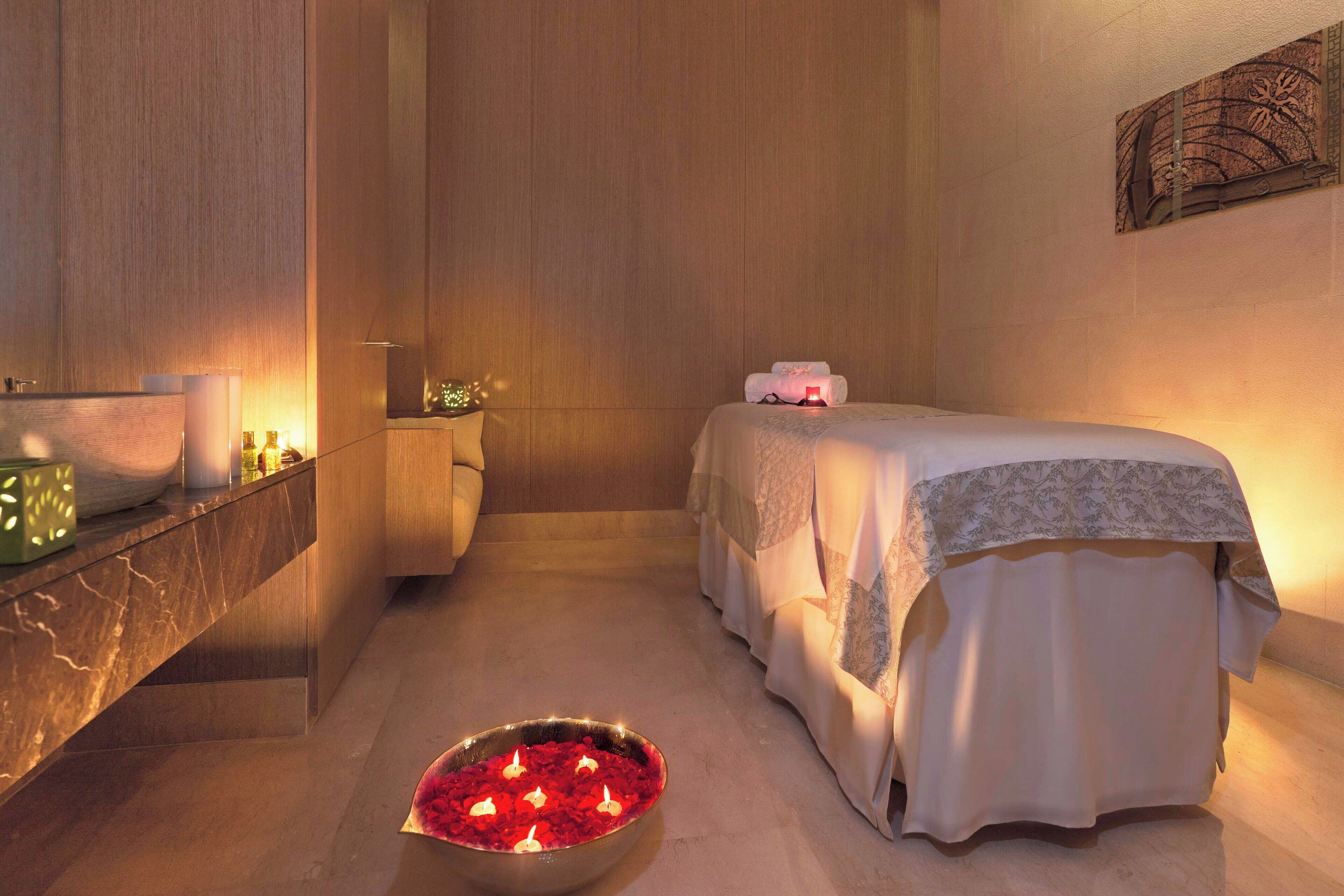 A spa room with a bed, a bowl of red flowers, and candles.