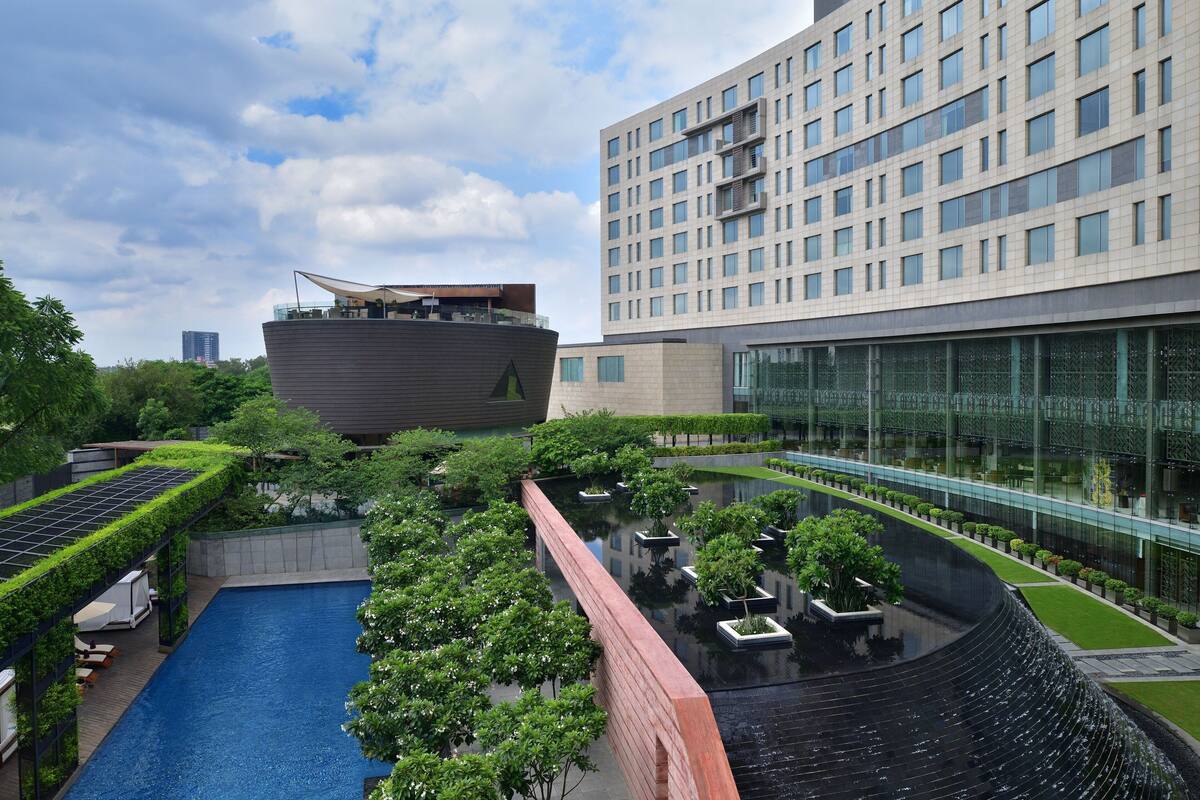 Um edifício moderno com piscina no terraço, rodeado por vegetação e fachada de vidro.