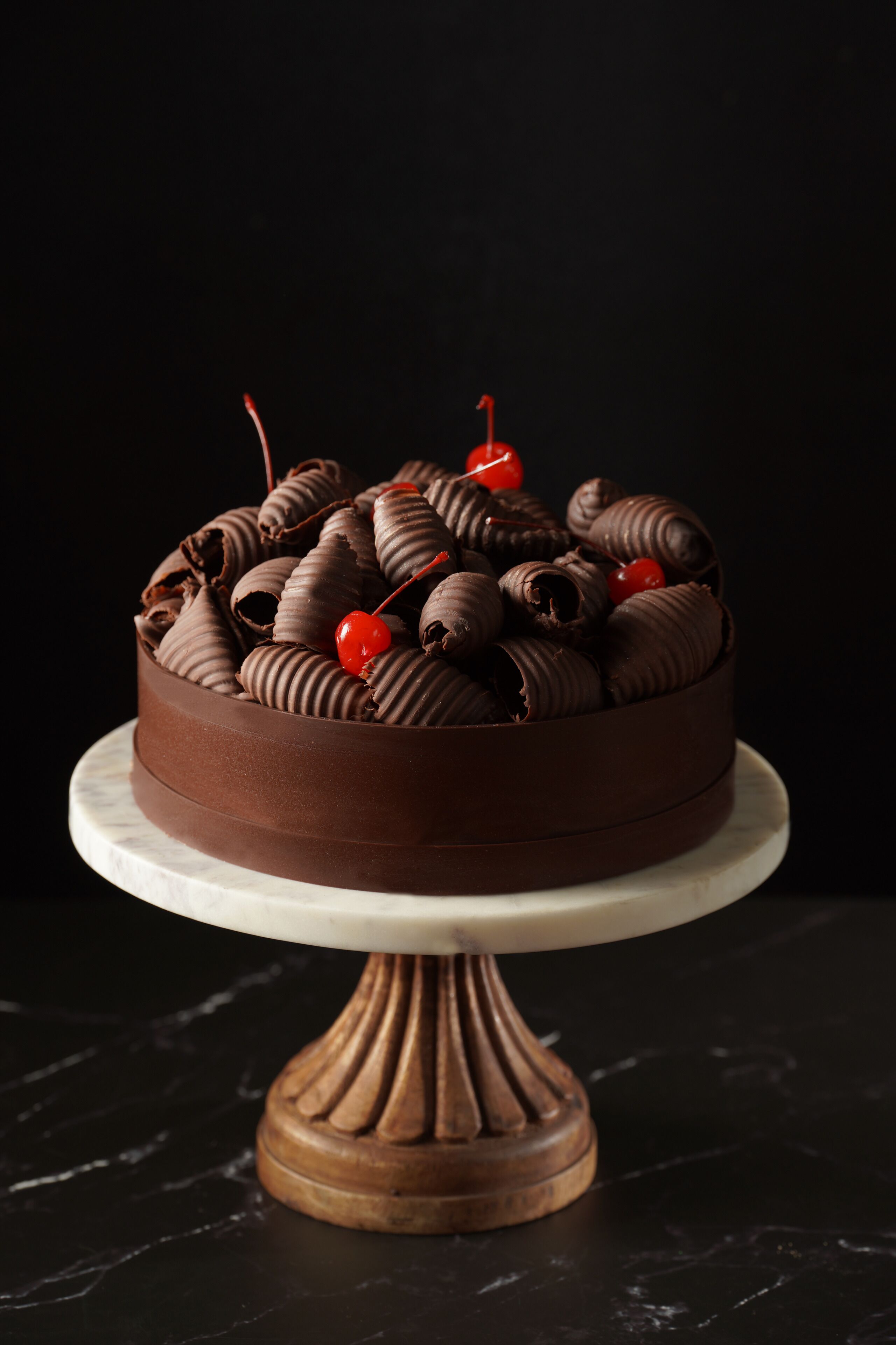 A chocolate cake with cherries on a marble cake stand.