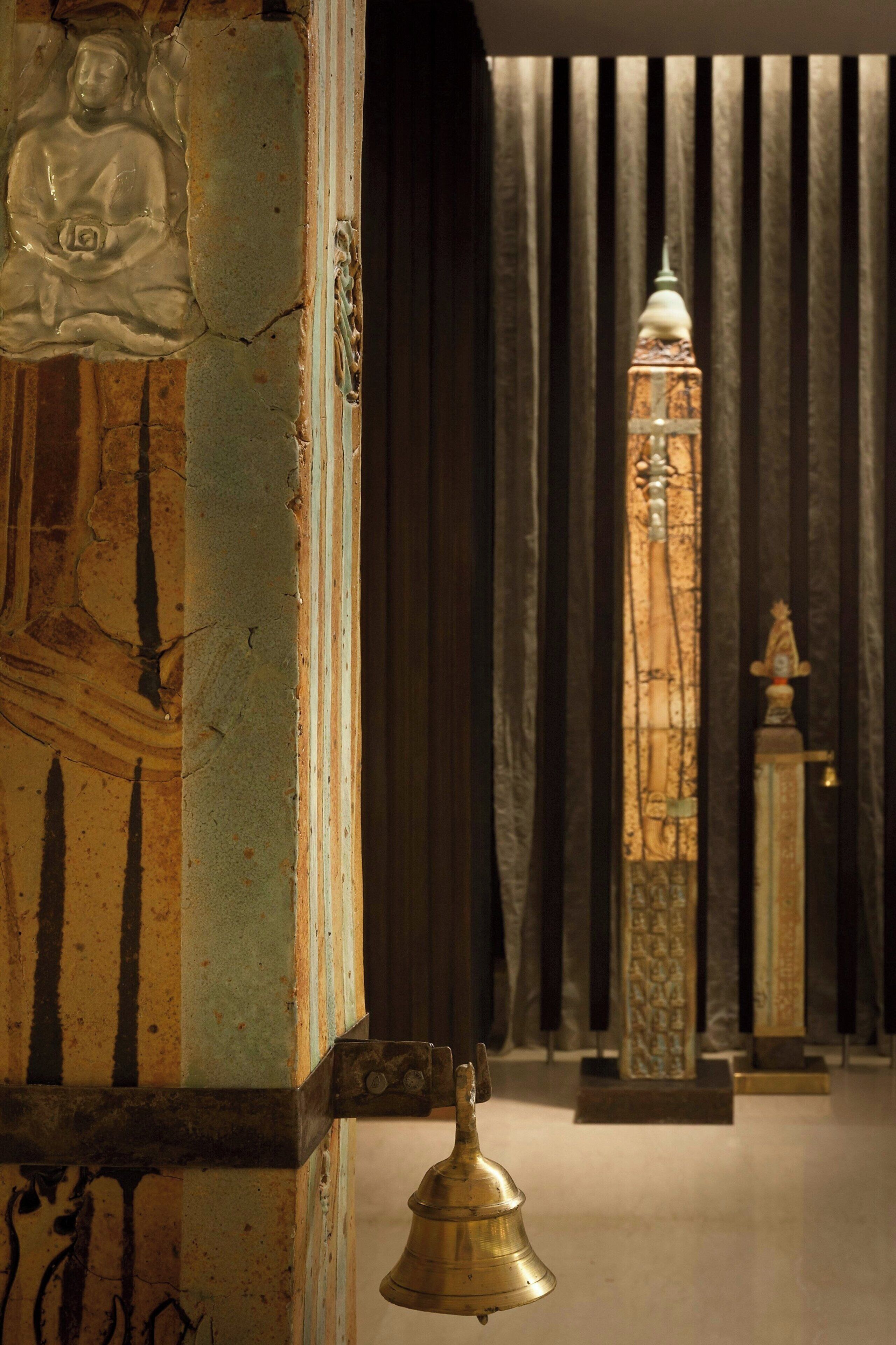 Une pièce avec une grande colonne richement décorée, une cloche et, au fond, une structure haute et étroite.