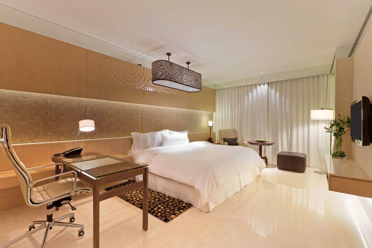 Quarto de hotel moderno com cama, escrivaninha, cadeira e televisão.