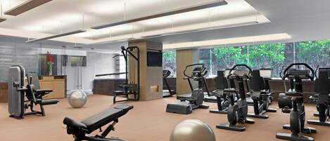 A modern gym with various exercise equipment, large windows, and a clean, spacious layout.