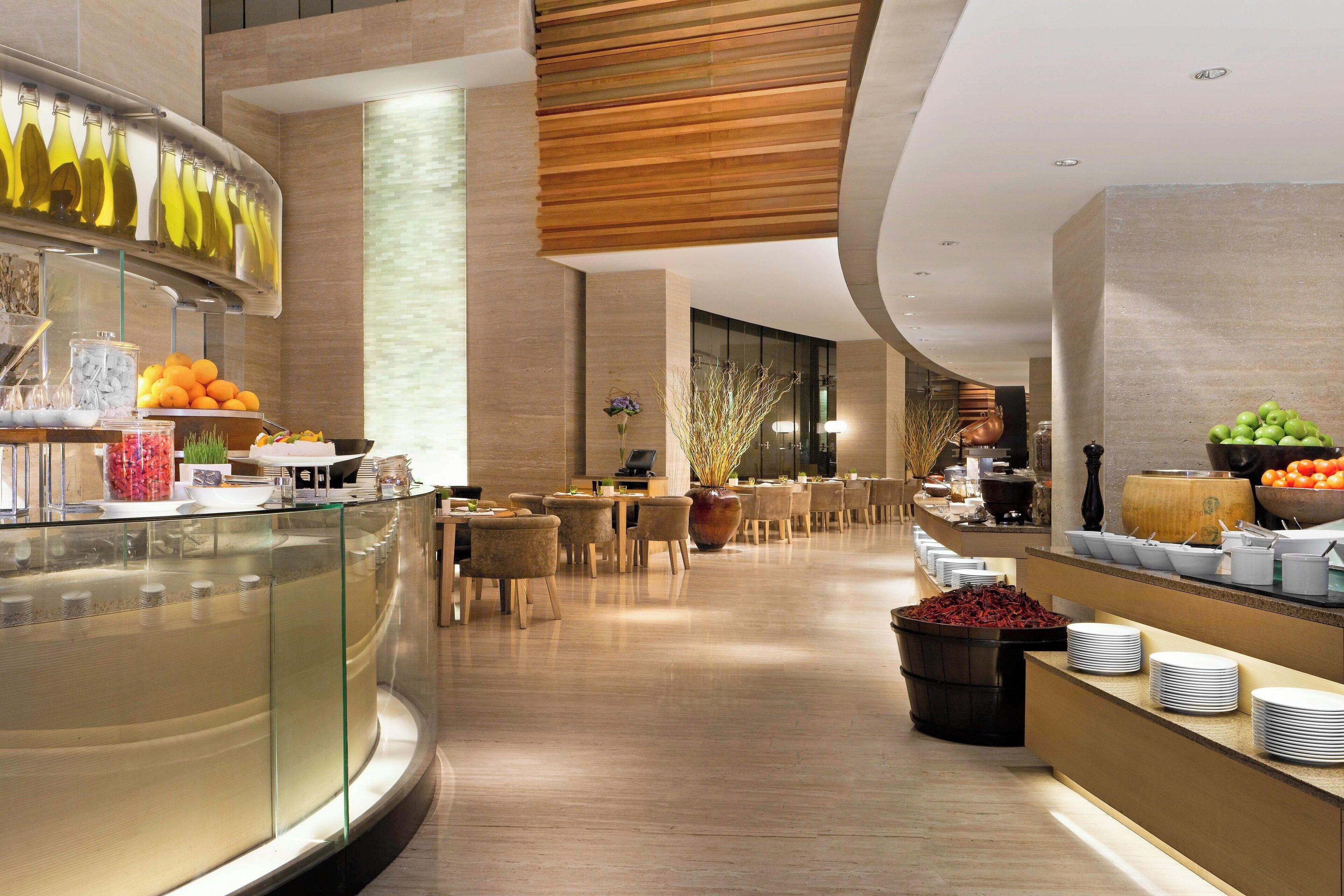 A modern hotel lobby with a buffet area, seating arrangements, and a large vase with dried plants.