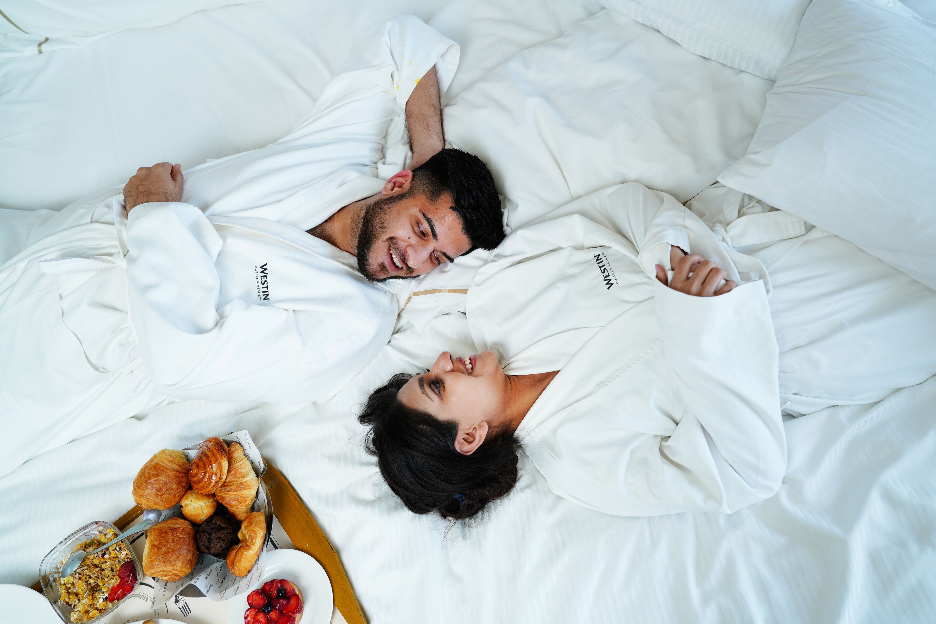 A bed with white bedding and a tray of pastries.