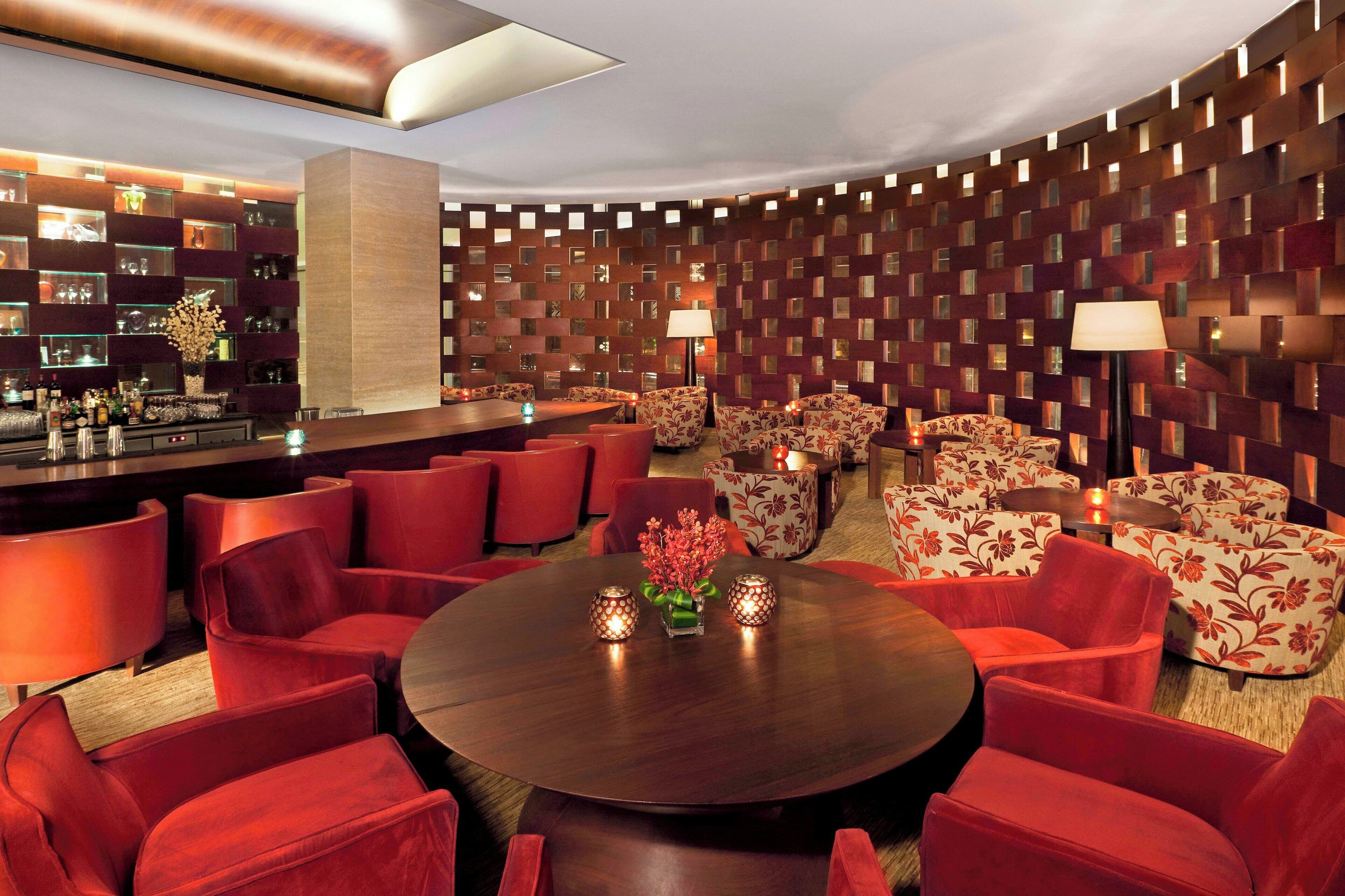 A modern lounge area with a round table, red upholstered chairs, and a patterned wall.