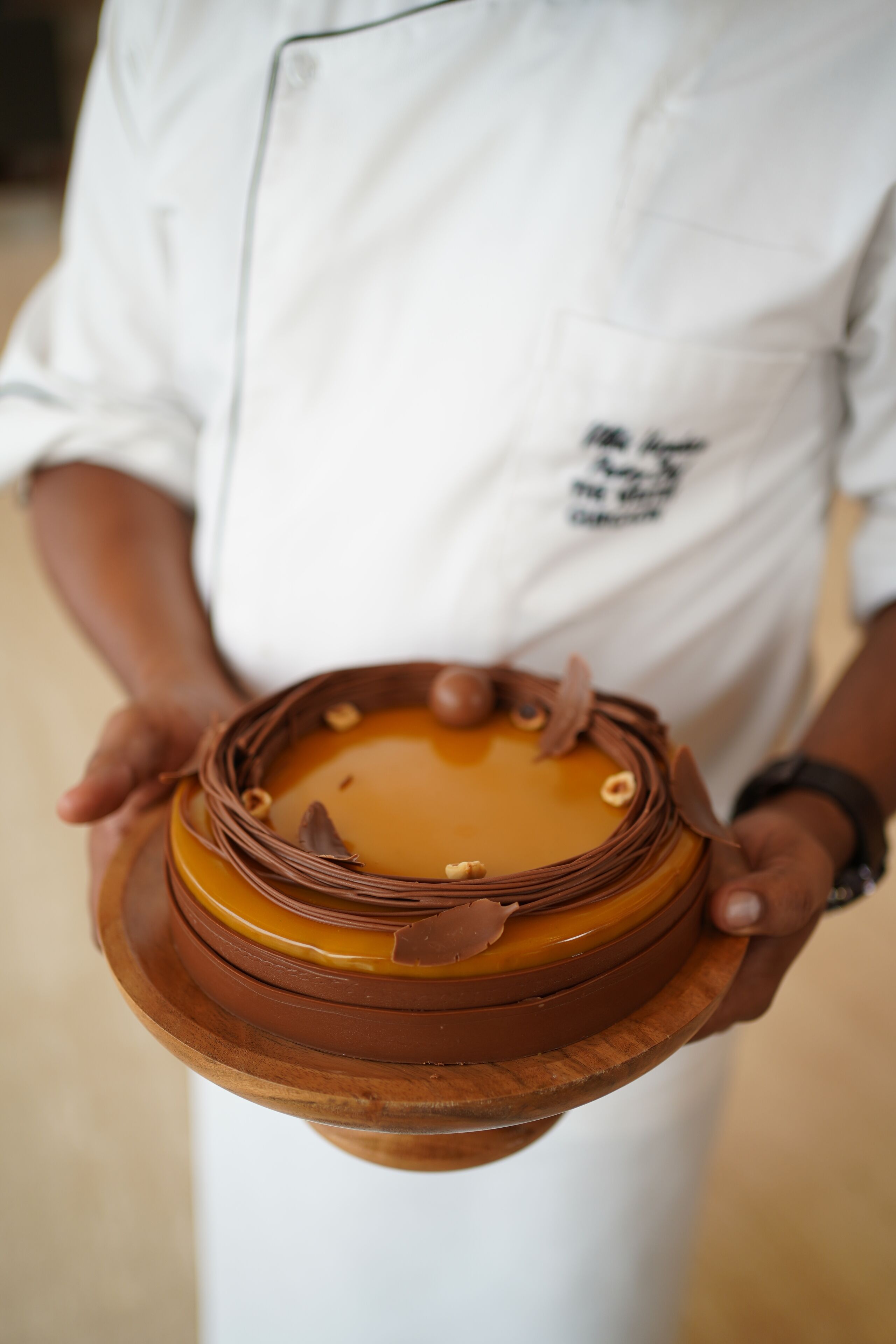A person holding a layered cake with a chocolate and caramel design.