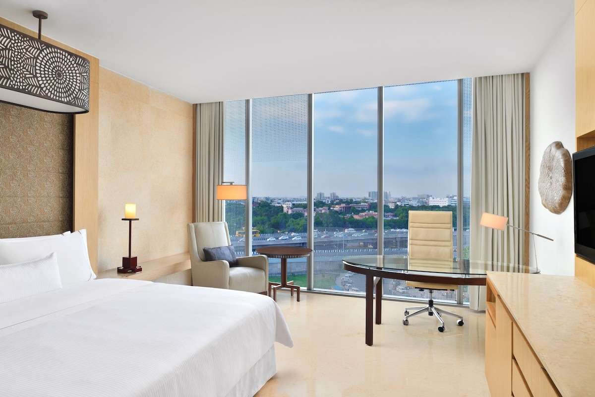 A hotel room with a large bed, a desk, a chair, and a view of the city.