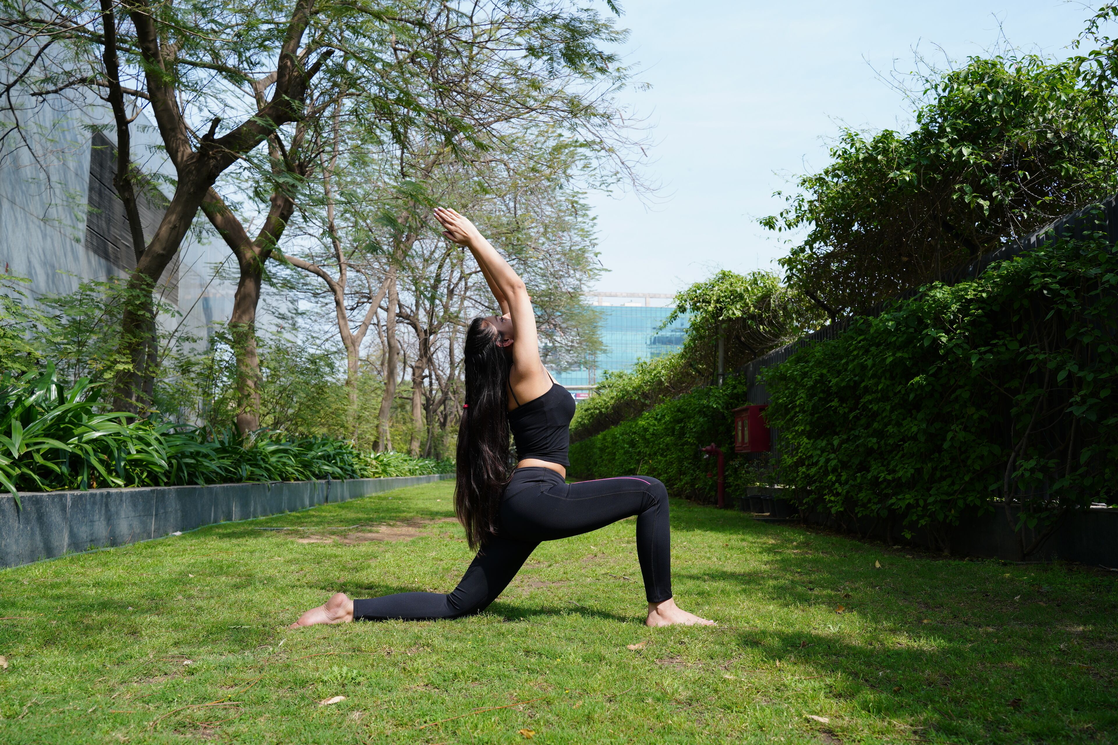 A person performing a yoga pose in a grassy outdoor area with trees and a building in the background.