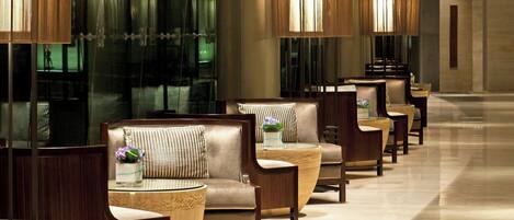 A modern hotel lobby with a long row of seating areas, a high ceiling, and a large, geometric wall structure.
