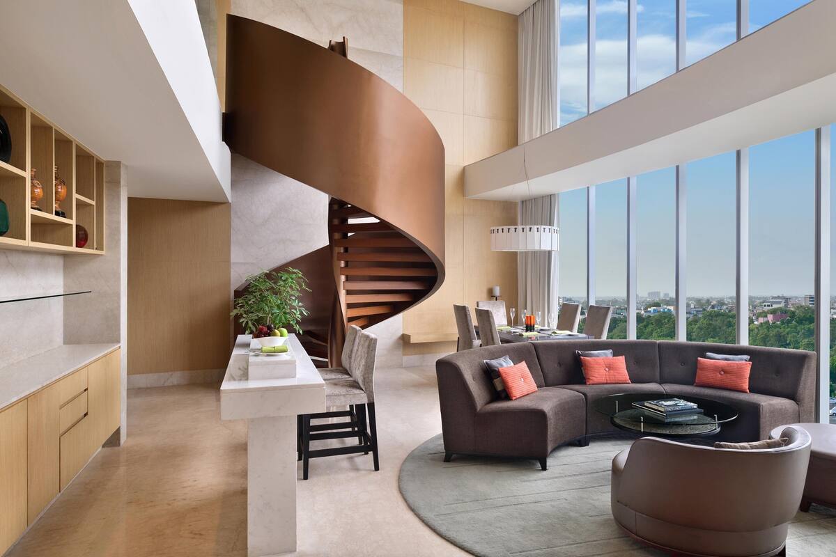 Uma sala de estar moderna com uma escada em curva, um conjunto de sofás e uma área de jantar com vista para a cidade.