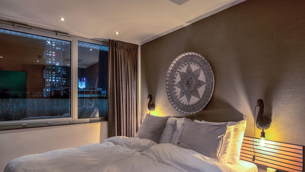Una habitación de hotel con una cama, un ventanal grande, una lámpara fijada a la pared y un adorno decorativo.