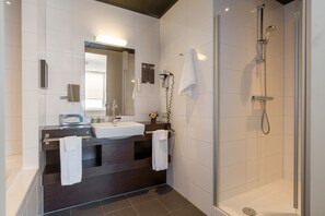 Un baño moderno con tocador de madera oscura, un espejo grande, lavabo integrado y ducha con mampara de vidrio.