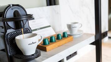 Een Nespresso koffieapparaat met een kop koffie die in een Vascobel kop wordt geserveerd, een houten kopjeshouder met extra kopjes, en een menukaart op de toonbank.