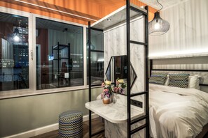 Un dormitorio moderno con cama, tocador con espejo y ventana con vista a la ciudad.