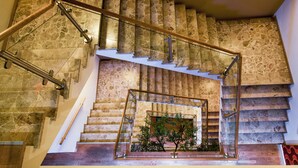 Una escalera de piedra de varios niveles con barandillas de cristal y pasamanos de madera.