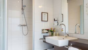 Un baño moderno con cabina de ducha de vidrio, un lavamanos blanco y un mueble de tocador de madera oscura.