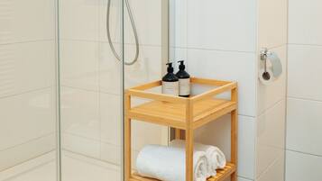 A shower with a glass door, a wooden shelf with towels, and toiletries.