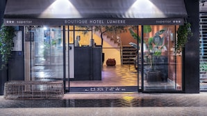 La entrada del Hotel Boutique Lumiere, con un diseño moderno, presenta un frente de vidrio, una escalera y una zona de recepción.
