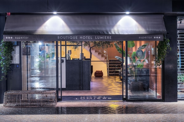 La entrada del Hotel Boutique Lumiere, con un diseño moderno, presenta un frente de vidrio, una escalera y una zona de recepción.