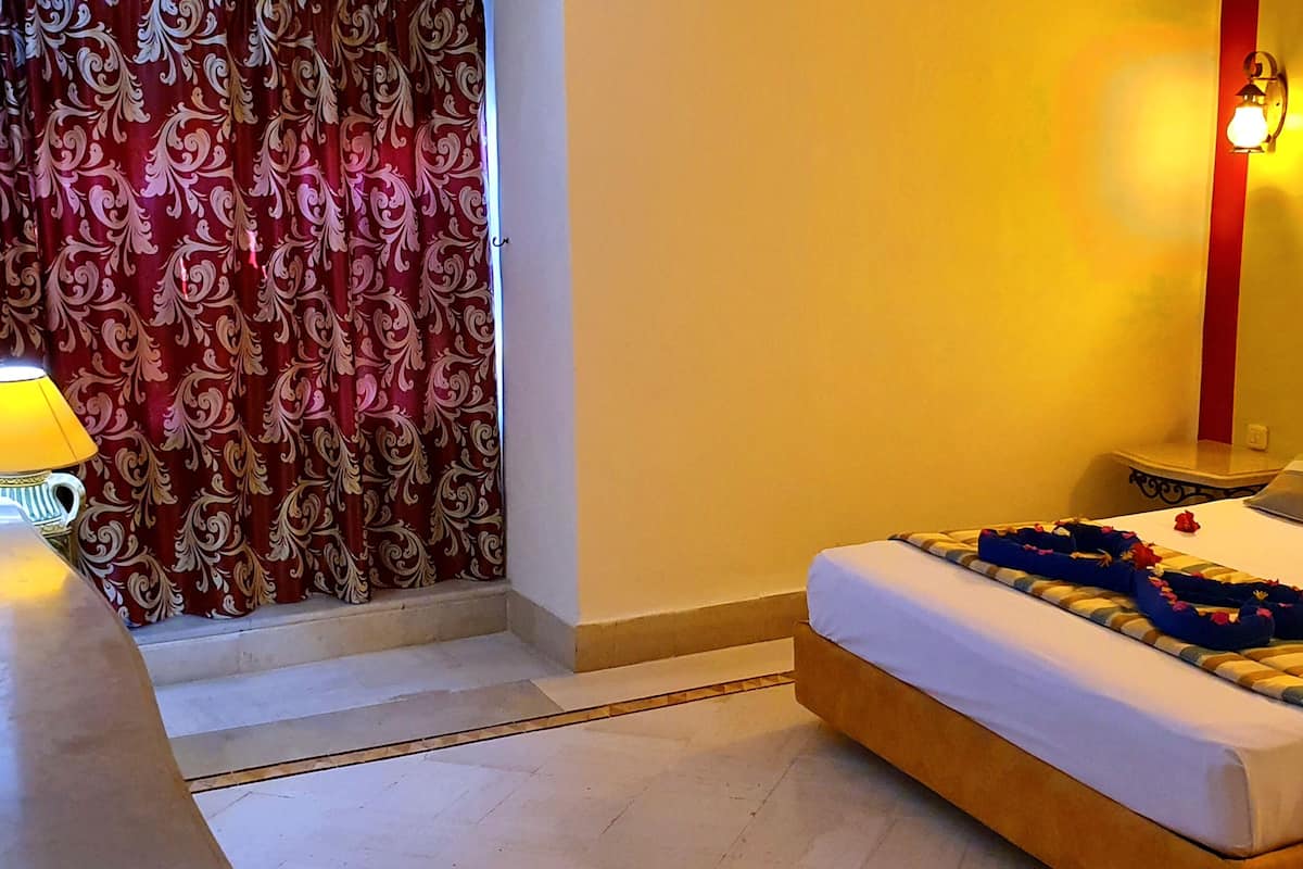 A hotel room with a bed, a TV, a lamp, and curtains.