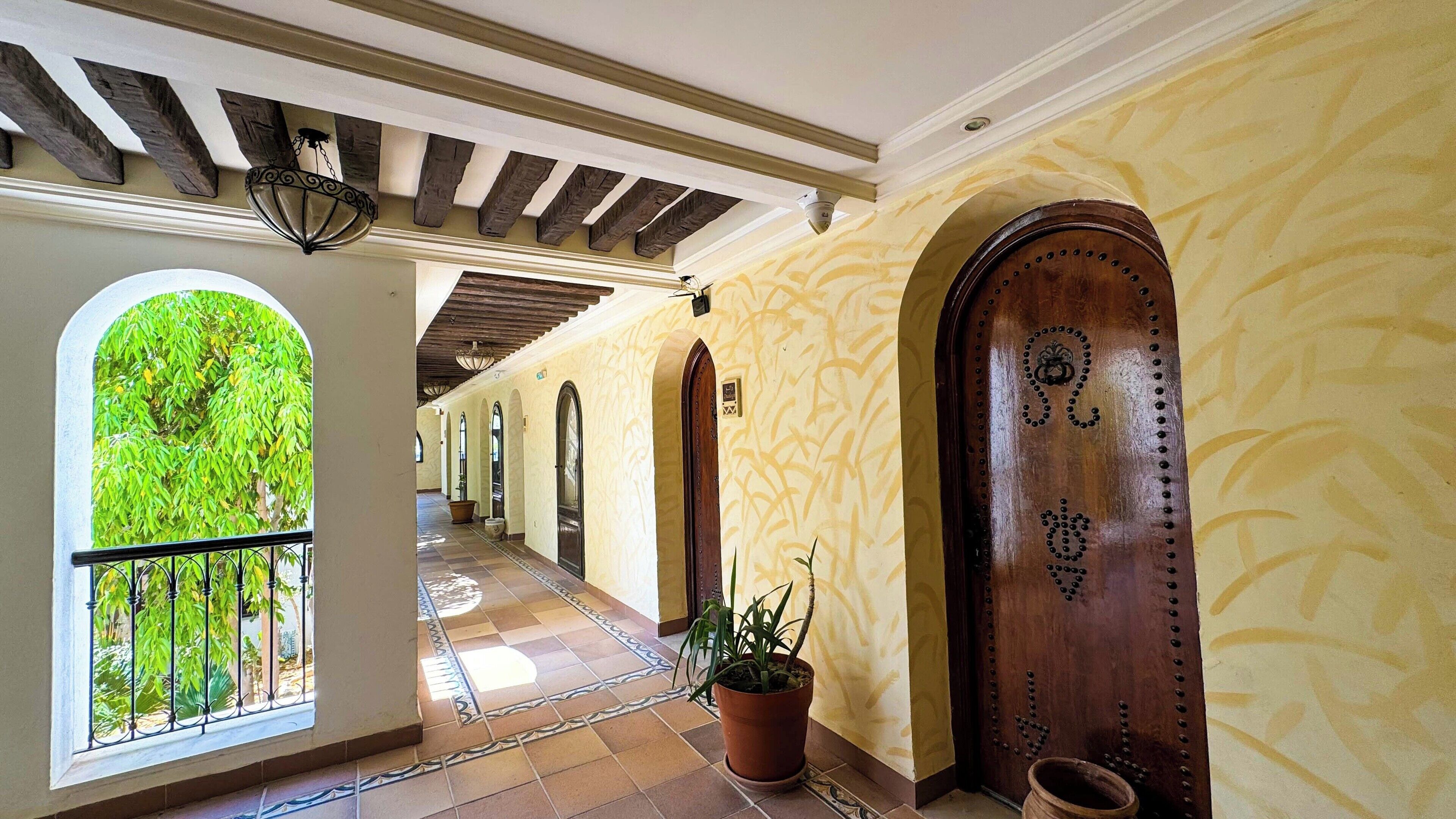 A corridor with arched doorways, a potted plant, and a tiled floor.