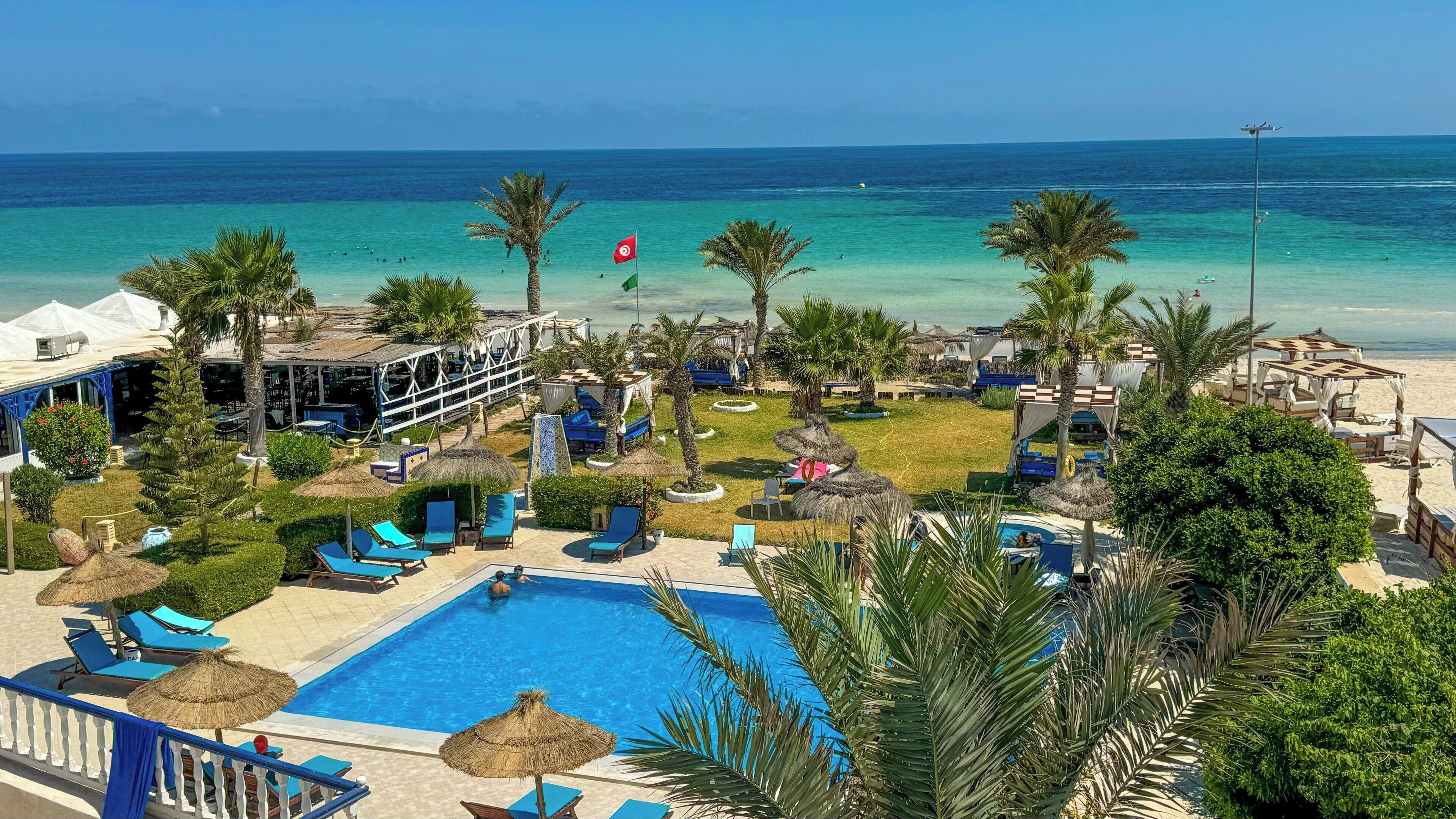 Um resort com piscina, guarda-sóis, espreguiçadeiras e vista para o mar.