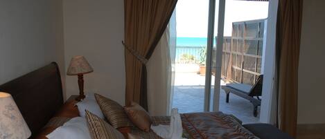 A hotel room with a bed, a lamp, and a view of the beach through a sliding door.
